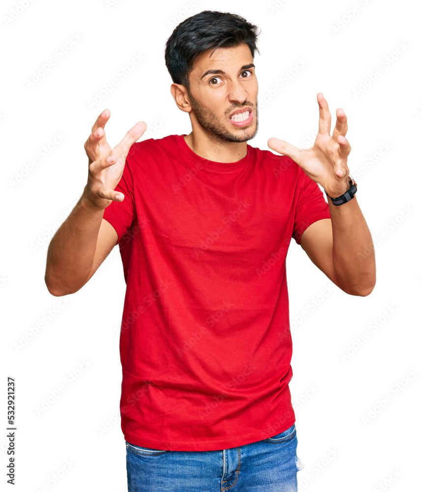 Fototapeta premium Young handsome man wearing casual red tshirt shouting frustrated with rage, hands trying to strangle, yelling mad