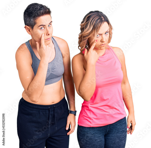 Couple of women wearing sportswear pointing to the eye watching you gesture, suspicious expression