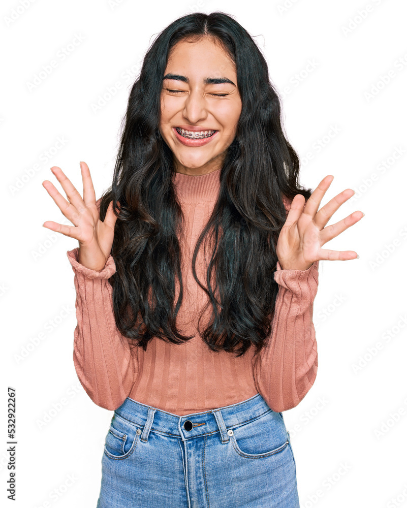 Hispanic teenager girl with dental braces wearing casual clothes celebrating mad and crazy for success with arms raised and closed eyes screaming excited. winner concept Hispanic teenager girl with dental braces wearing casual clothes celebrating mad and crazy for success with arms raised and closed eyes screaming excited. winner concept