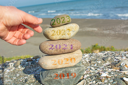 New Year 2023 is coming concept. Old year 2022 change to 2023 background. Turn of old year concept. Happy new year 2023 replace 2022. New hopes, excitement with 2023. Man adding stone to pebble tower.