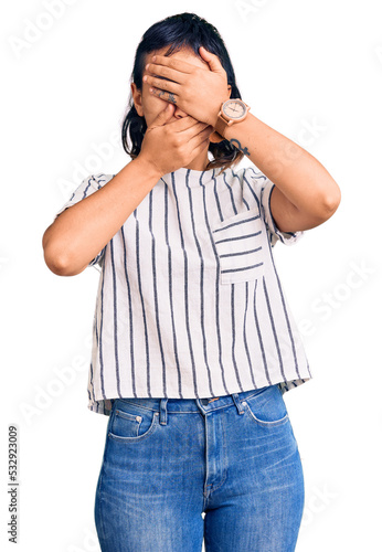 Young woman wearing casual clothes covering eyes and mouth with hands, surprised and shocked. hiding emotion