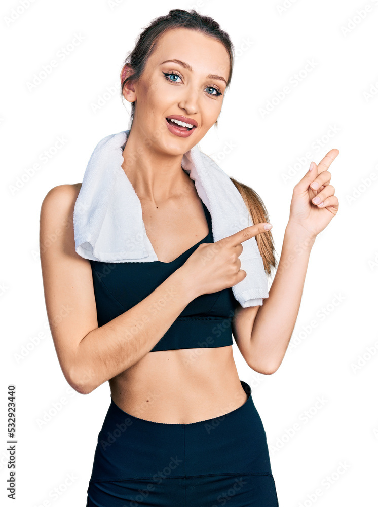 Beautiful caucasian woman wearing sportswear and towel smiling and looking at the camera pointing with two hands and fingers to the side.