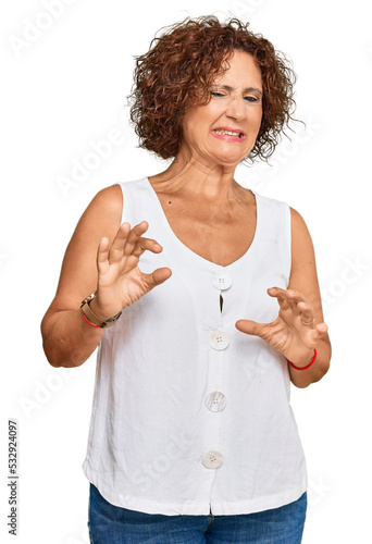 Beautiful middle age mature woman wearing casual white shirt disgusted expression, displeased and fearful doing disgust face because aversion reaction. with hands raised