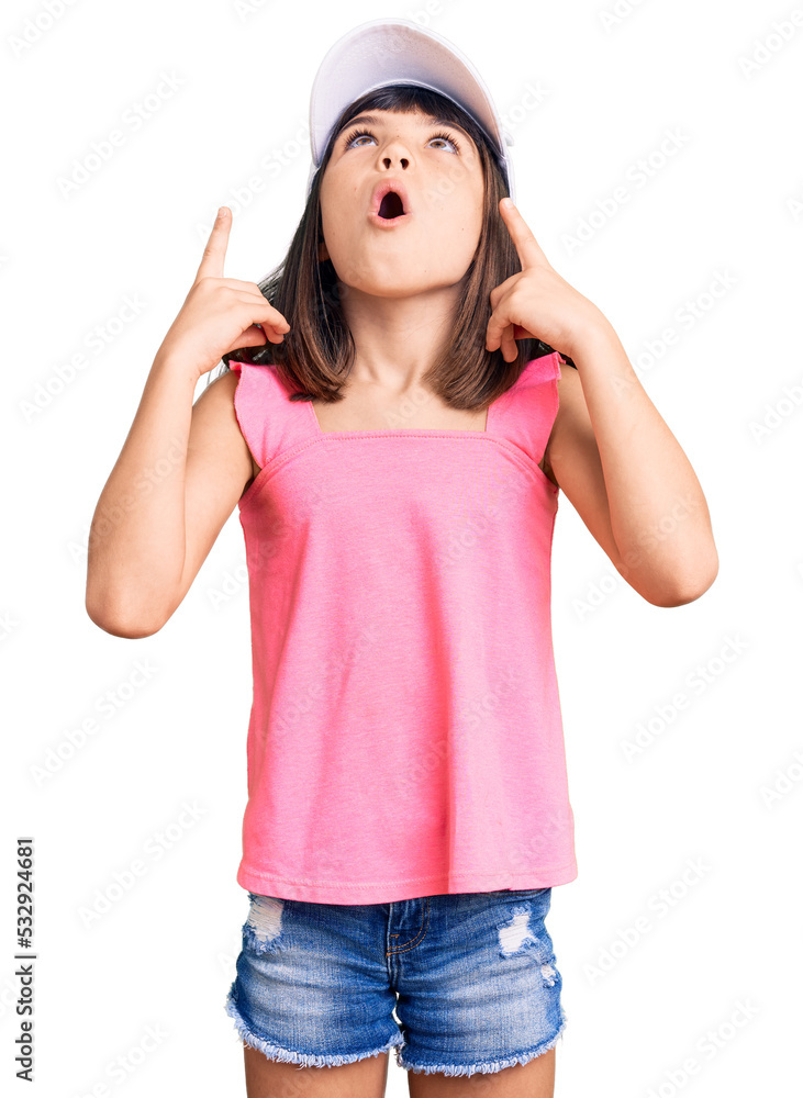 Young little girl with bang wearing funny kitty cap amazed and surprised looking up and pointing with fingers and raised arms. Young little girl with bang wearing funny kitty cap amazed and surprised looking up and pointing with fingers and raised arms.
