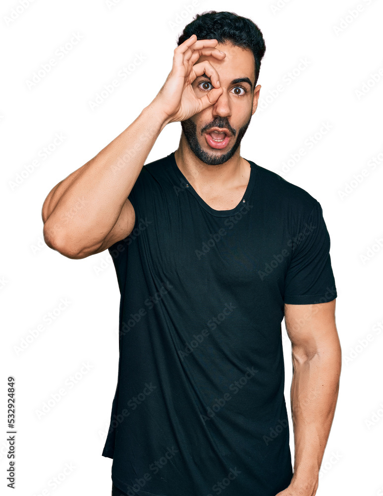 Hispanic man with beard wearing casual black t shirt doing ok gesture shocked with surprised face, eye looking through fingers. unbelieving expression. Hispanic man with beard wearing casual black t shirt doing ok gesture shocked with surprised face, eye looking through fingers. unbelieving expression.