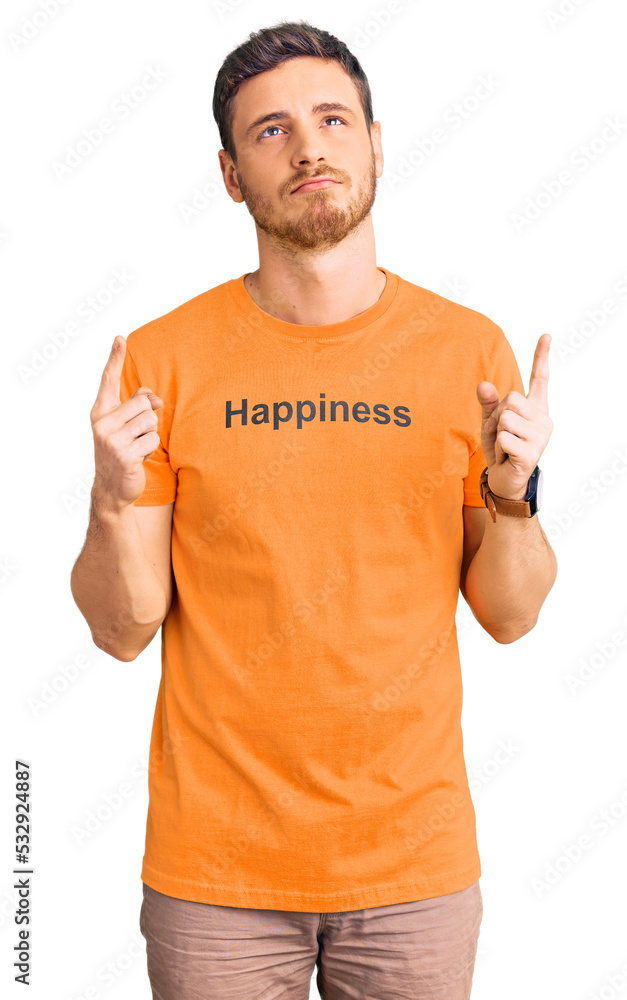 Handsome young man with bear wearing tshirt with happiness word message pointing up looking sad and upset, indicating direction with fingers, unhappy and depressed. Handsome young man with bear wearing tshirt with happiness word message pointing up looking sad and upset, indicating direction with fingers, unhappy and depressed.