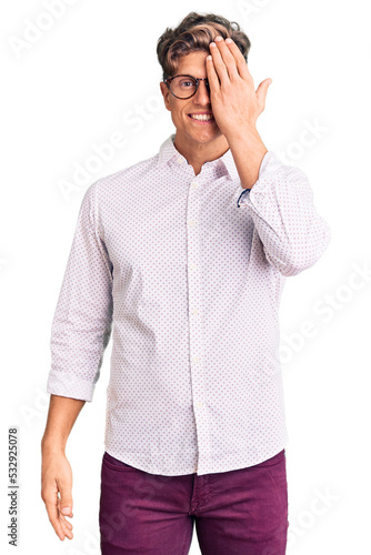 Young handsome man wearing business clothes and glasses covering one eye with hand, confident smile on face and surprise emotion.