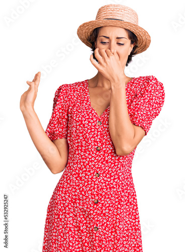 Photography Young beautiful woman wearing summer hat smelling something stinky and disgusting, intolerable smell, holding breath with fingers on nose