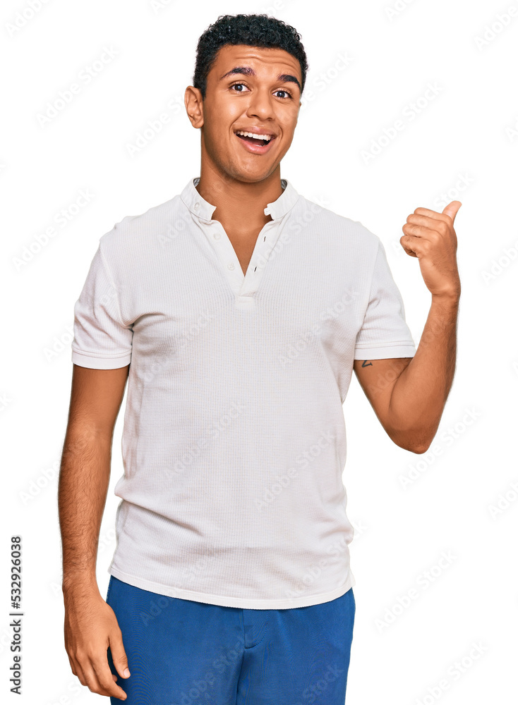 Young arab man wearing casual clothes smiling with happy face looking and pointing to the side with thumb up. Young arab man wearing casual clothes smiling with happy face looking and pointing to the side with thumb up.