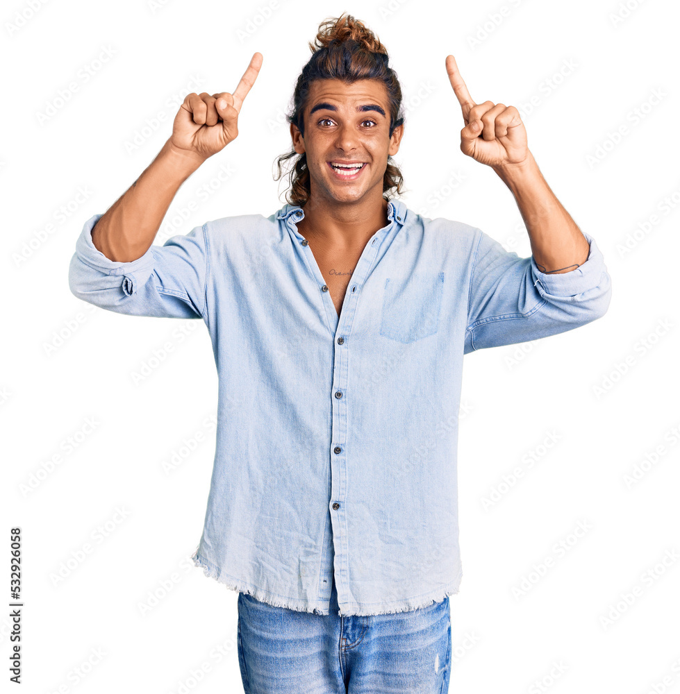 Young hispanic man wearing summer style smiling amazed and surprised and pointing up with fingers and raised arms. Young hispanic man wearing summer style smiling amazed and surprised and pointing up with fingers and raised arms.
