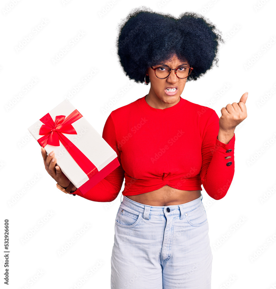 Young african american girl holding gift angry and mad raising fist frustrated and furious while shouting with anger. rage and aggressive concept. Young african american girl holding gift angry and mad raising fist frustrated and furious while shouting with anger. rage and aggressive concept.