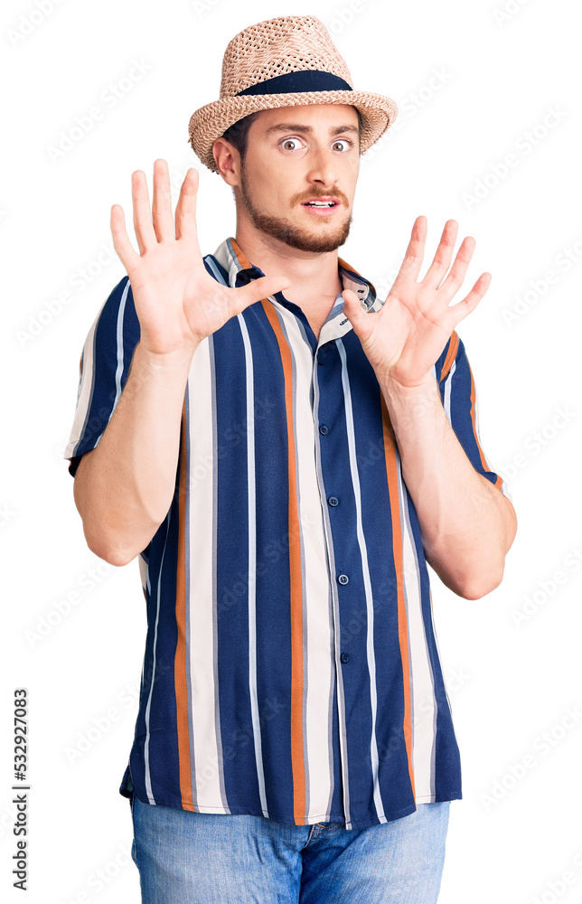 Young handsome caucasian man wearing summer hat afraid and terrified with fear expression stop gesture with hands, shouting in shock. panic concept. Young handsome caucasian man wearing summer hat afraid and terrified with fear expression stop gesture with hands, shouting in shock. panic concept.