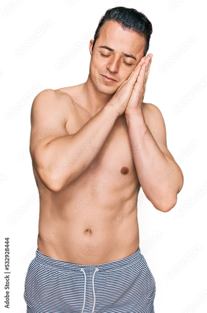 Fototapeta premium Handsome young man wearing swimwear shirtless sleeping tired dreaming and posing with hands together while smiling with closed eyes.