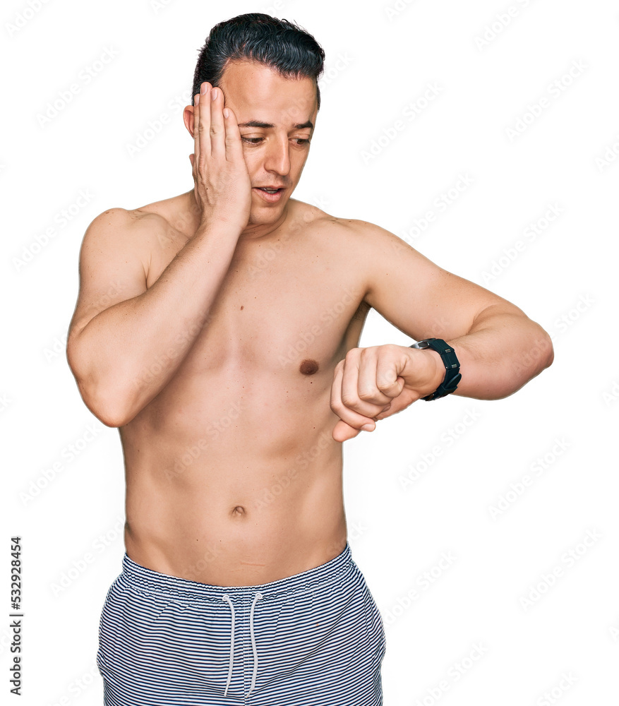 Handsome young man wearing swimwear shirtless looking at the watch time worried, afraid of getting late Handsome young man wearing swimwear shirtless looking at the watch time worried, afraid of getting late
