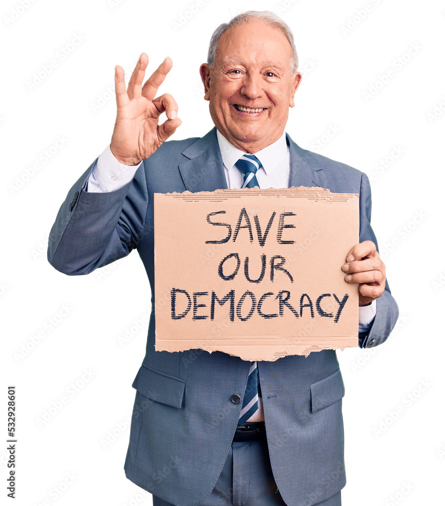 Senior handsome grey-haired man holding save our democracy cardboard banner doing ok sign with fingers, smiling friendly gesturing excellent symbol Senior handsome grey-haired man holding save our democracy cardboard banner doing ok sign with fingers, smiling friendly gesturing excellent symbol