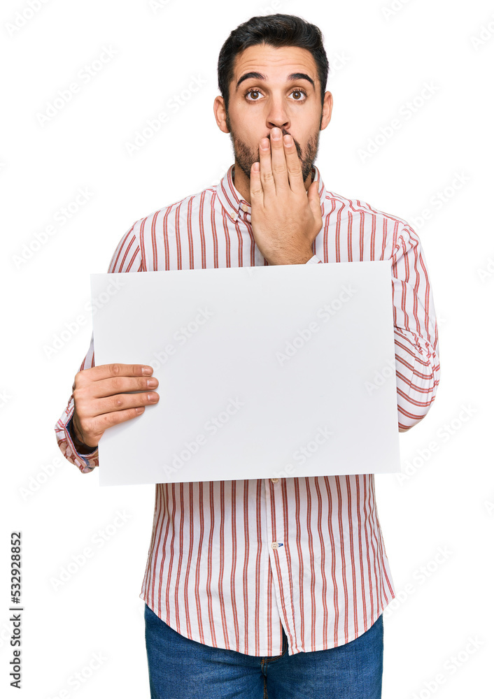 Young hispanic man holding blank empty banner covering mouth with hand, shocked and afraid for mistake. surprised expression Young hispanic man holding blank empty banner covering mouth with hand, shocked and afraid for mistake. surprised expression