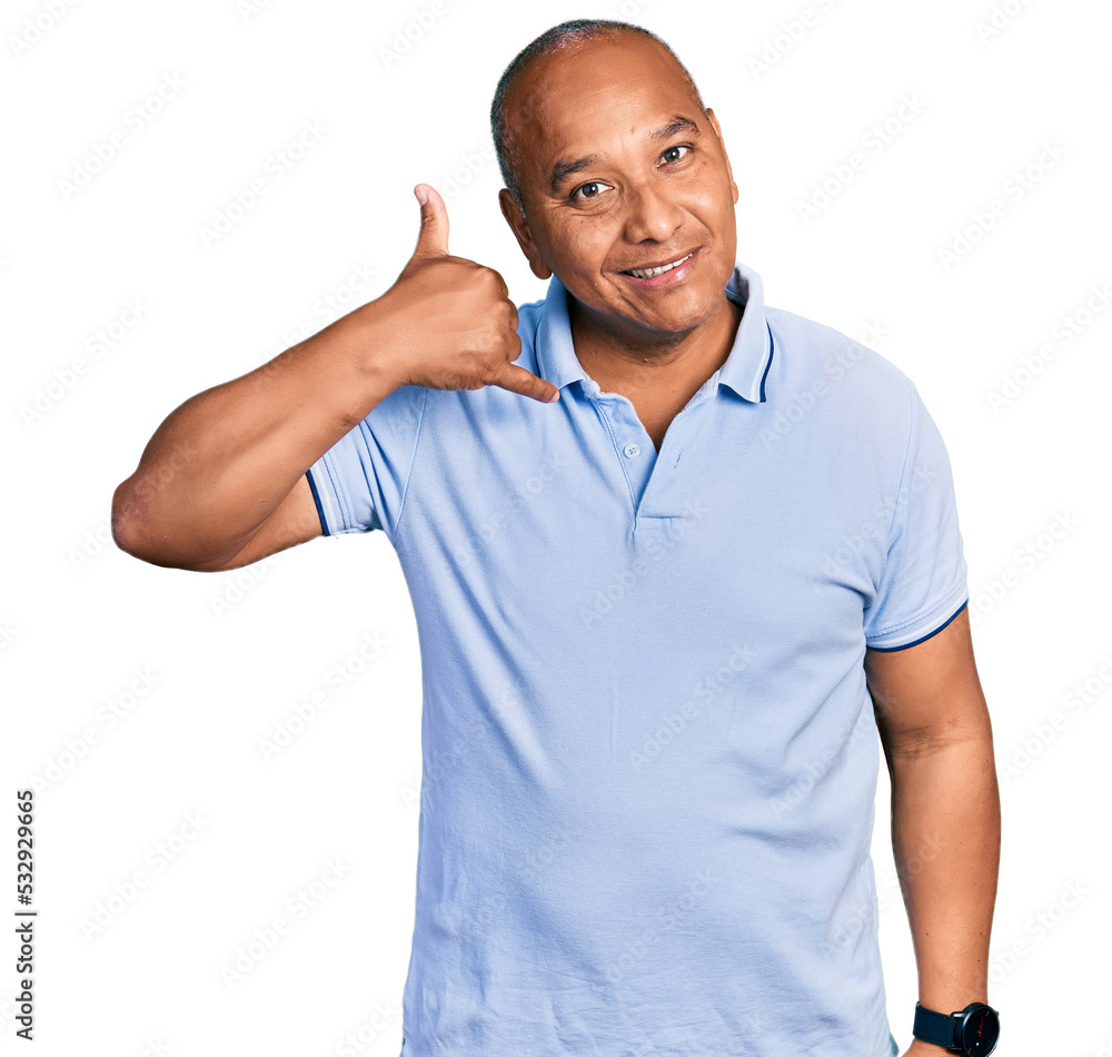 Hispanic middle age man wearing casual t shirt smiling doing phone gesture with hand and fingers like talking on the telephone. communicating concepts. Hispanic middle age man wearing casual t shirt smiling doing phone gesture with hand and fingers like talking on the telephone. communicating concepts.