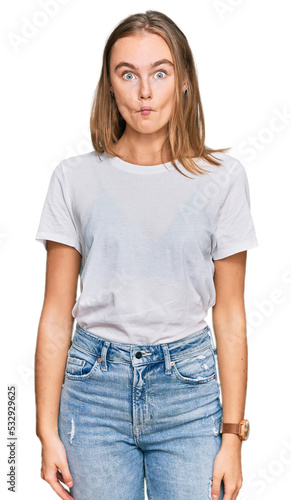 Beautiful young blonde woman wearing casual white t shirt making fish face with lips, crazy and comical gesture. funny expression.