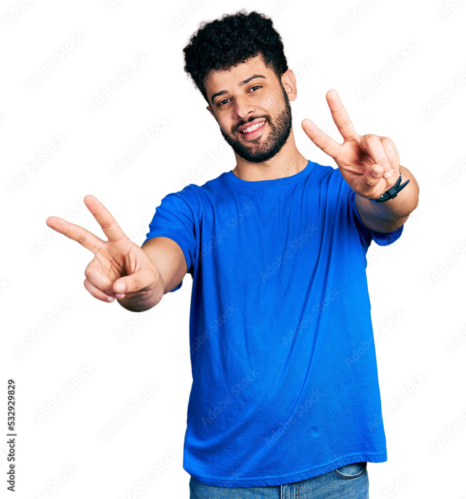 Young arab man with beard wearing casual blue t shirt smiling with tongue out showing fingers of both hands doing victory sign. number two. Young arab man with beard wearing casual blue t shirt smiling with tongue out showing fingers of both hands doing victory sign. number two.