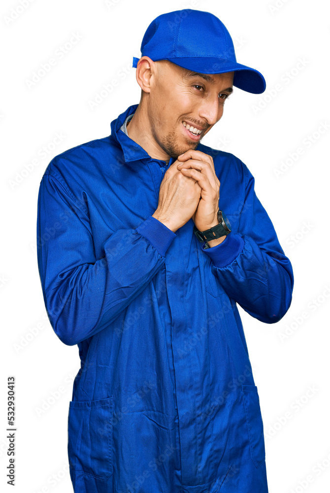 Bald man with beard wearing builder jumpsuit uniform laughing nervous and excited with hands on chin looking to the side Bald man with beard wearing builder jumpsuit uniform laughing nervous and excited with hands on chin looking to the side