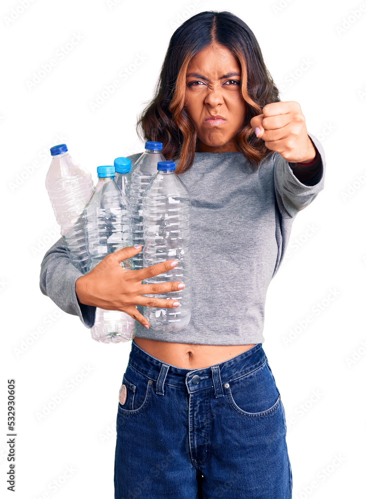 Young beautiful mixed race woman holding recycling plastic bottles annoyed and frustrated shouting with anger, yelling crazy with anger and hand raised Young beautiful mixed race woman holding recycling plastic bottles annoyed and frustrated shouting with anger, yelling crazy with anger and hand raised