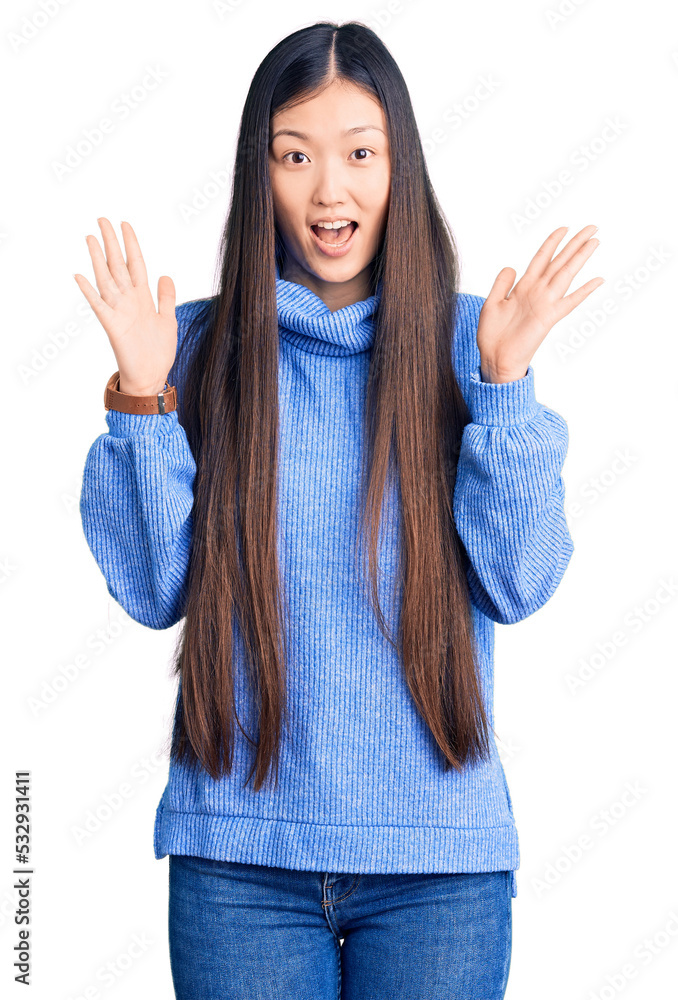 Young beautiful chinese woman wearing casual turtleneck sweater celebrating crazy and amazed for success with arms raised and open eyes screaming excited. winner concept Young beautiful chinese woman wearing casual turtleneck sweater celebrating crazy and amazed for success with arms raised and open eyes screaming excited. winner concept
