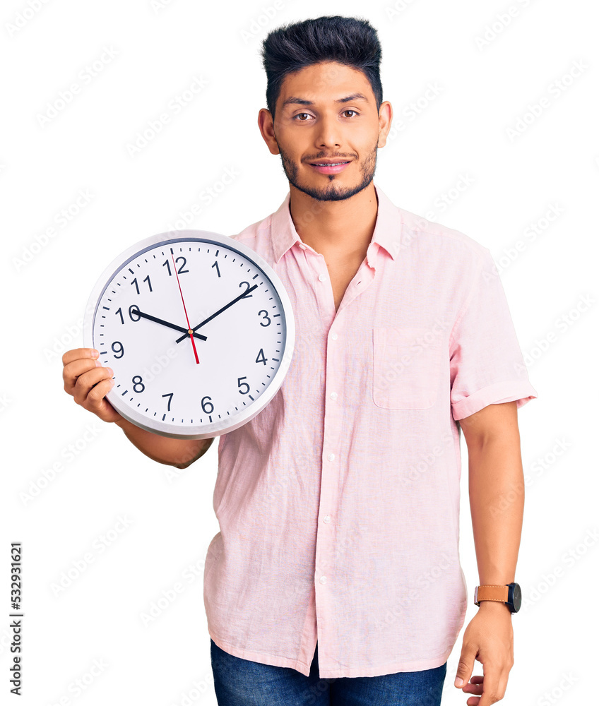 Handsome latin american young man holding big clock looking positive and happy standing and smiling with a confident smile showing teeth Handsome latin american young man holding big clock looking positive and happy standing and smiling with a confident smile showing teeth