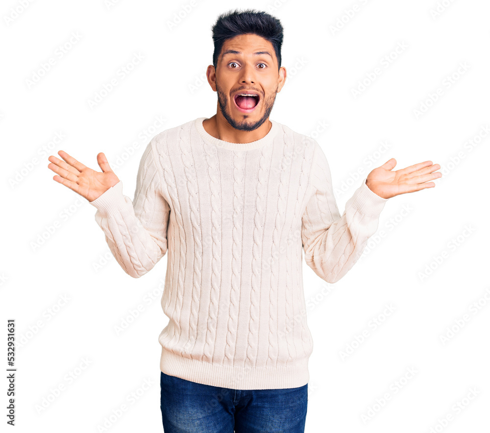 Handsome latin american young man wearing casual winter sweater celebrating victory with happy smile and winner expression with raised hands Handsome latin american young man wearing casual winter sweater celebrating victory with happy smile and winner expression with raised hands