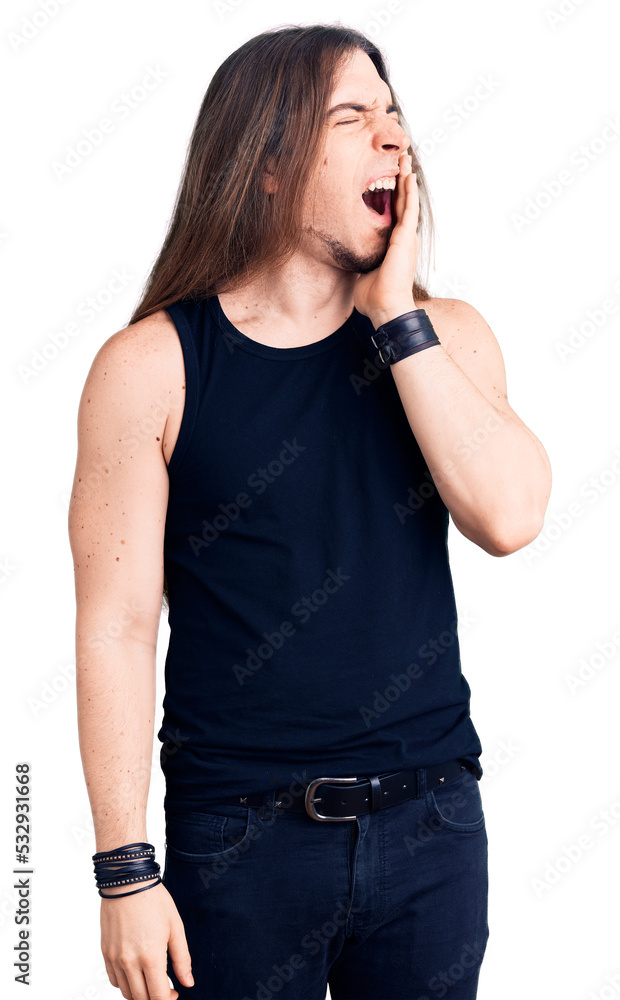 Young adult man with long hair wearing goth style with black clothes bored yawning tired covering mouth with hand. restless and sleepiness. Young adult man with long hair wearing goth style with black clothes bored yawning tired covering mouth with hand. restless and sleepiness.