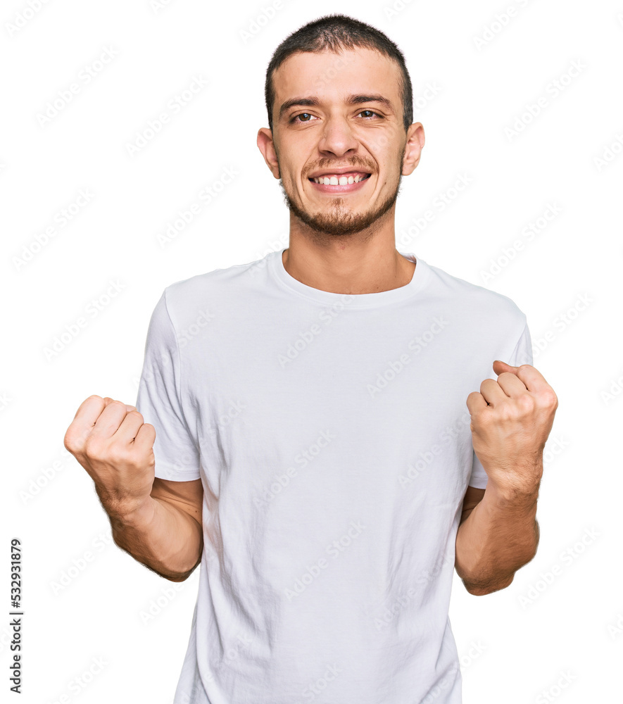 Hispanic young man wearing casual white t shirt excited for success with arms raised and eyes closed celebrating victory smiling. winner concept. Hispanic young man wearing casual white t shirt excited for success with arms raised and eyes closed celebrating victory smiling. winner concept.