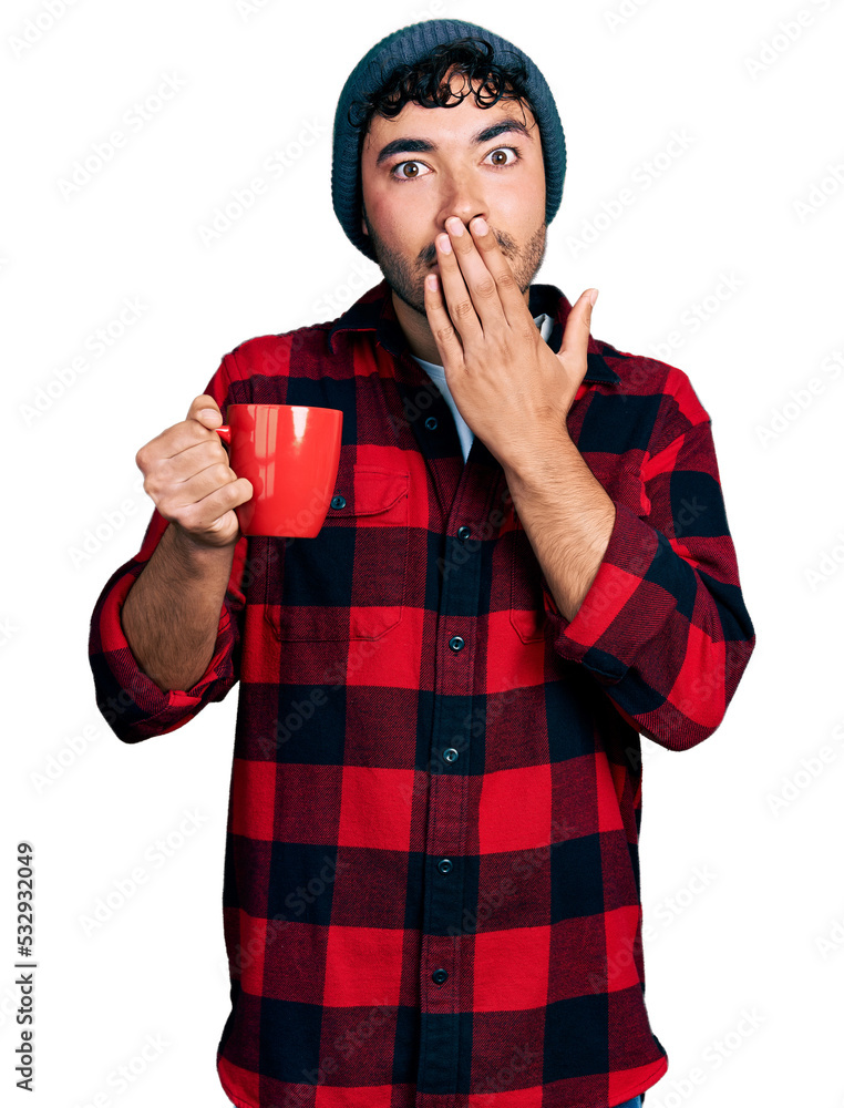 Hispanic young man with beard drinking a cup of coffee covering mouth with hand, shocked and afraid for mistake. surprised expression Hispanic young man with beard drinking a cup of coffee covering mouth with hand, shocked and afraid for mistake. surprised expression