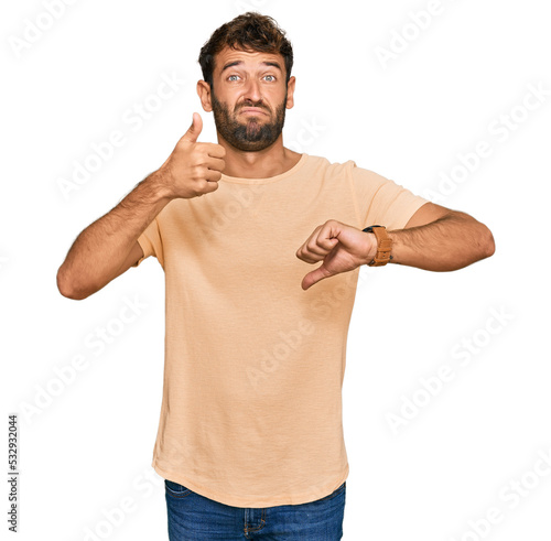 Handsome young man with beard wearing casual tshirt doing thumbs up and down, disagreement and agreement expression. crazy conflict