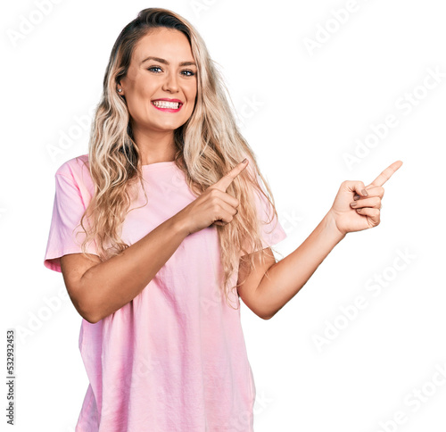 Foto Young blonde woman wearing casual pink t shirt smiling and looking at the camera pointing with two hands and fingers to the side