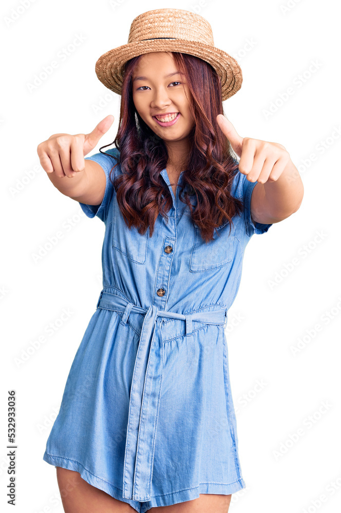 Young beautiful chinese girl wearing summer hat approving doing positive gesture with hand, thumbs up smiling and happy for success. winner gesture. Young beautiful chinese girl wearing summer hat approving doing positive gesture with hand, thumbs up smiling and happy for success. winner gesture.