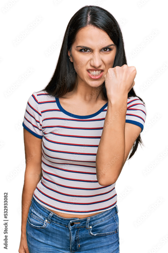 Young hispanic girl wearing casual striped t shirt angry and mad raising fist frustrated and furious while shouting with anger. rage and aggressive concept. Young hispanic girl wearing casual striped t shirt angry and mad raising fist frustrated and furious while shouting with anger. rage and aggressive concept.