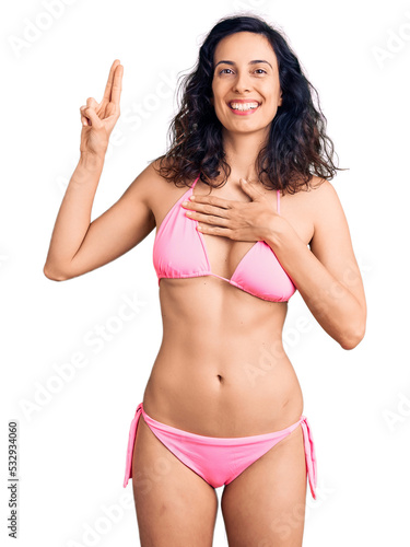 Young beautiful hispanic woman wearing bikini smiling swearing with hand on chest and fingers up, making a loyalty promise oath © Krakenimages.com