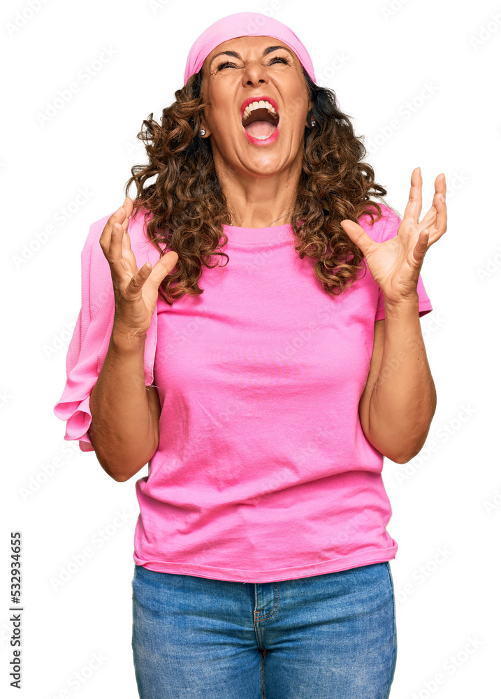 Middle age hispanic woman wearing breast cancer support pink scarf crazy and mad shouting and yelling with aggressive expression and arms raised. frustration concept. Middle age hispanic woman wearing breast cancer support pink scarf crazy and mad shouting and yelling with aggressive expression and arms raised. frustration concept.
