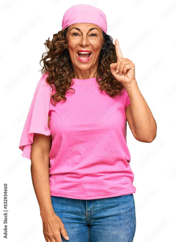 Middle age hispanic woman wearing breast cancer support pink scarf pointing finger up with successful idea. exited and happy. number one. Middle age hispanic woman wearing breast cancer support pink scarf pointing finger up with successful idea. exited and happy. number one.