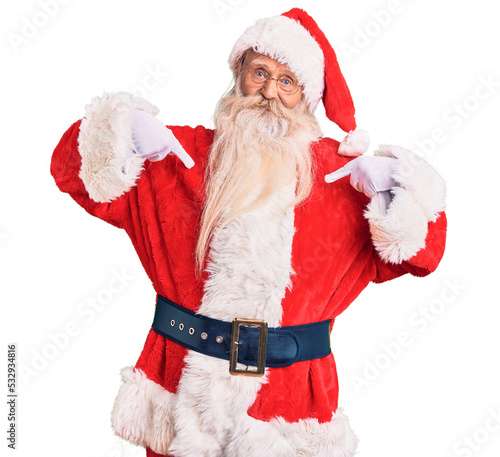 Old senior man with grey hair and long beard wearing traditional santa claus costume looking confident with smile on face, pointing oneself with fingers proud and happy.