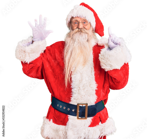 Old senior man with grey hair and long beard wearing traditional santa claus costume showing and pointing up with fingers number six while smiling confident and happy.