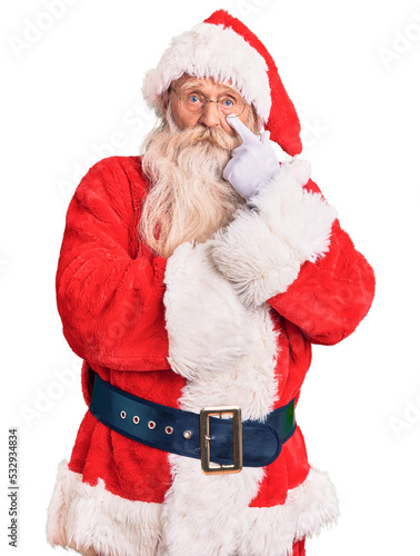 Old senior man with grey hair and long beard wearing traditional santa claus costume pointing to the eye watching you gesture, suspicious expression