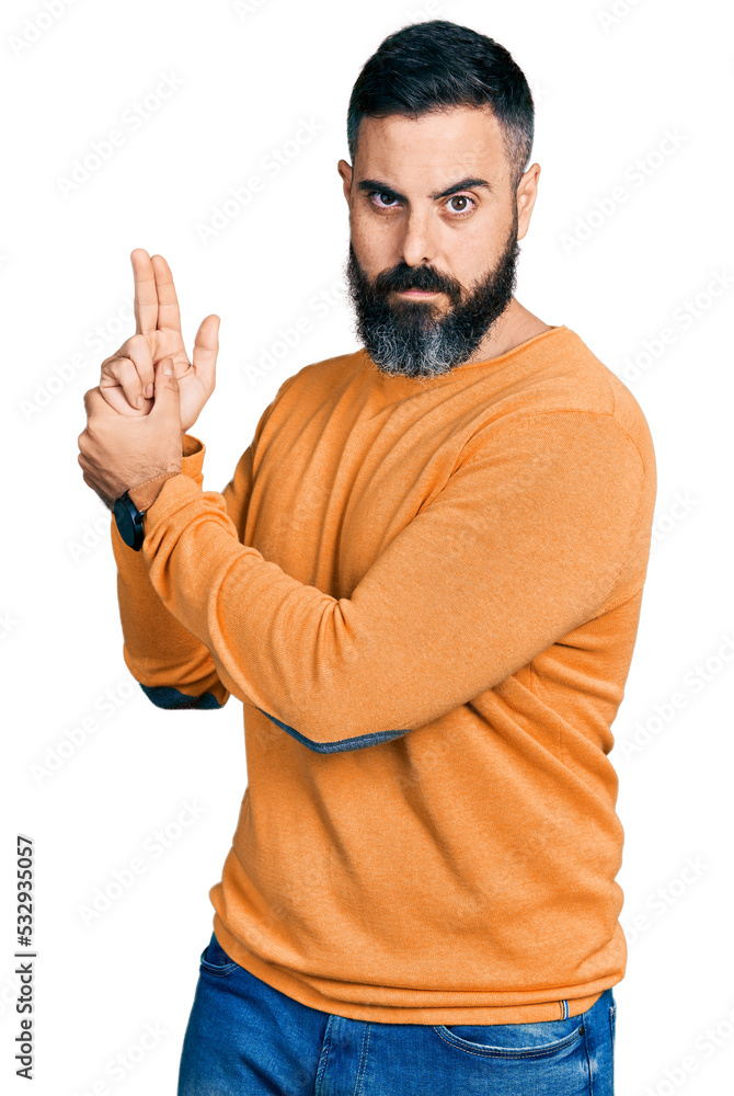Fototapeta premium Hispanic man with beard wearing casual winter sweater holding symbolic gun with hand gesture, playing killing shooting weapons, angry face