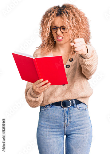 Young blonde woman with curly hair wearing glasses and reading book annoyed and frustrated shouting with anger, yelling crazy with anger and hand raised