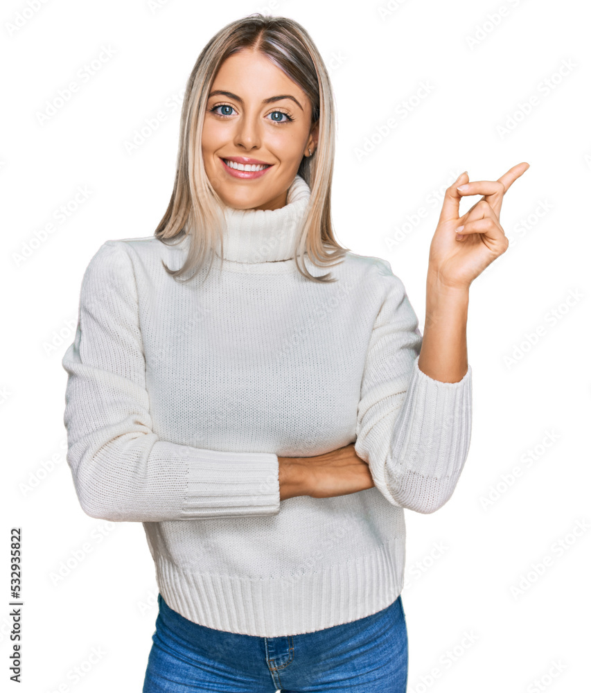 Obraz premium Beautiful blonde woman wearing casual turtleneck sweater with a big smile on face, pointing with hand and finger to the side looking at the camera.