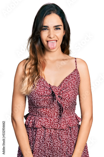 Beautiful hispanic woman wearing summer dress sticking tongue out happy with funny expression. emotion concept.