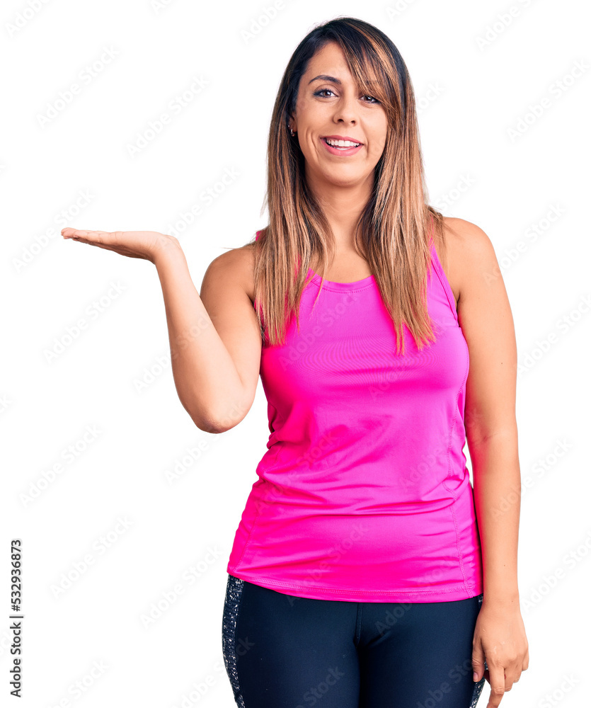 Young beautiful woman wearing sportswear smiling cheerful presenting and pointing with palm of hand looking at the camera. Young beautiful woman wearing sportswear smiling cheerful presenting and pointing with palm of hand looking at the camera.