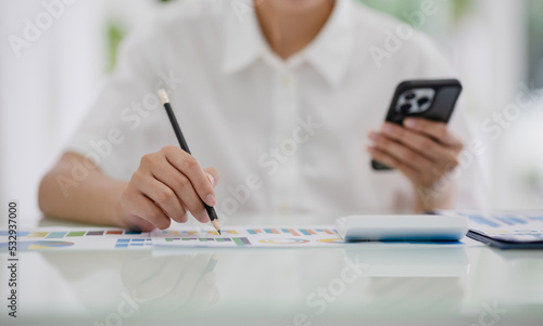 Asian woman at desk using smartphone financial app and doing reports close hand in hand.