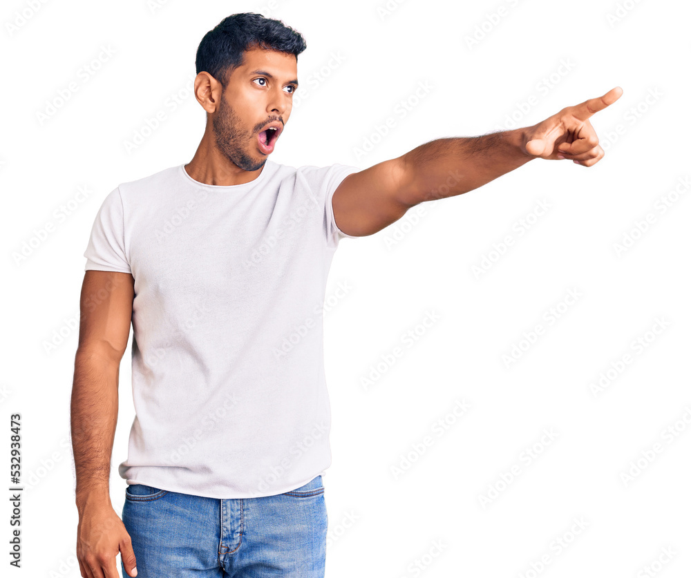 Young latin man wearing casual clothes pointing with finger surprised ahead, open mouth amazed expression, something on the front Young latin man wearing casual clothes pointing with finger surprised ahead, open mouth amazed expression, something on the front