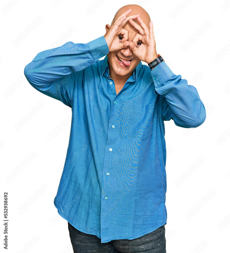 Middle age bald man wearing casual clothes doing ok gesture like binoculars sticking tongue out, eyes looking through fingers. crazy expression. Middle age bald man wearing casual clothes doing ok gesture like binoculars sticking tongue out, eyes looking through fingers. crazy expression.