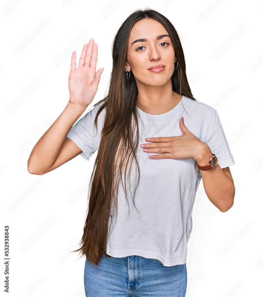 Young hispanic girl wearing casual white t shirt swearing with hand on chest and open palm, making a loyalty promise oath Young hispanic girl wearing casual white t shirt swearing with hand on chest and open palm, making a loyalty promise oath